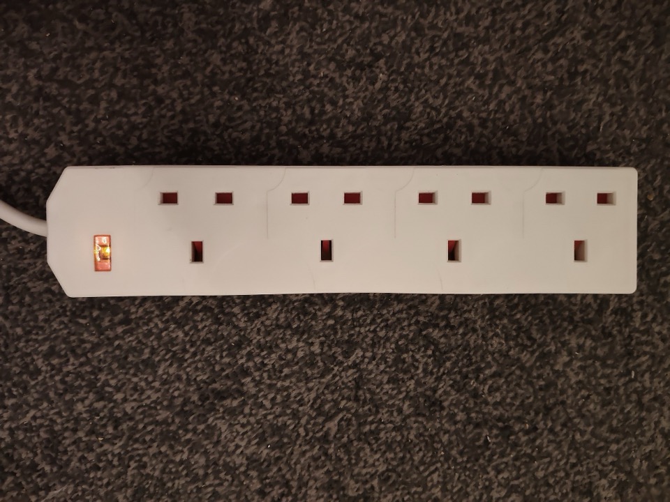 A white four way extension block with UK sockets lying on a carpet